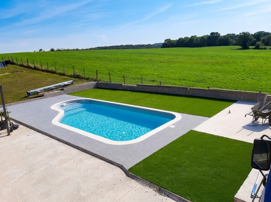 Piscine coque polyester de forme romaine installée en extérieur, entourée d'un dallage en béton désactivé gris